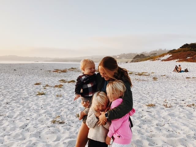 A host mom on the beach at sunset, holding her three young children close.